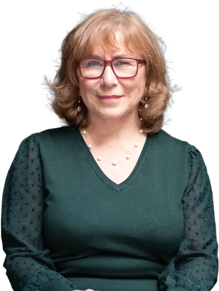 A person with shoulder-length hair and glasses wears a dark green top and a pearl necklace, exuding calmness akin to a serene therapy session. The plain background subtly echoes the tranquility often sought in NYC's bustling environment.