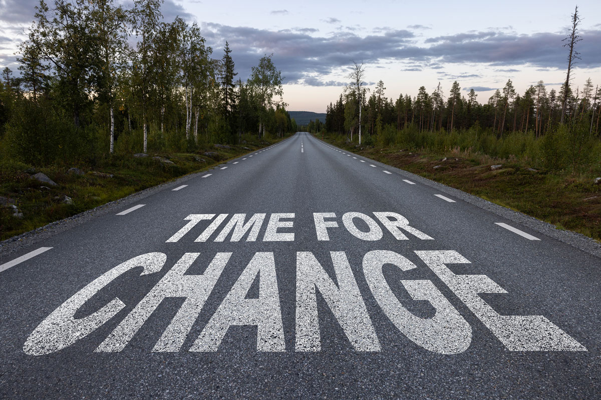 A long, straight road surrounded by trees with "Time for Change" painted in large, white letters across the asphalt under a partly cloudy sky evokes a journey as transformative as therapy. It's as if this serene path holds the promise of renewal far from NYC's bustling streets.