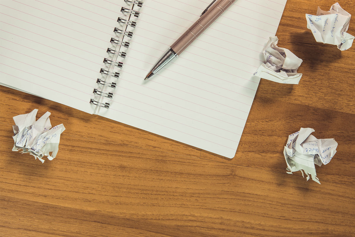 A spiral notebook lies open on a wooden table with a pen resting on it, much like the endless rewrite of ideas during therapy sessions. Crumpled pieces of paper are scattered around, mirroring the city's vibrant yet chaotic energy reminiscent of NYC.